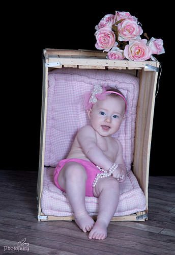 תינוקת יושבת בארגז עם פרחים